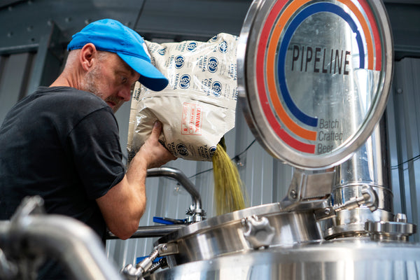 pipeline brewing co head brewer jonny cooper pouring hops into a brew
