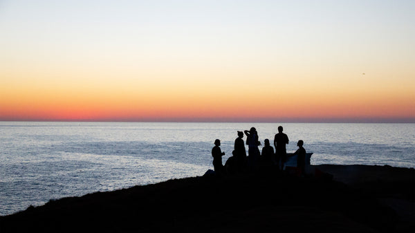 silhouette of a group of friends drinking beers watching the sunset into the sea